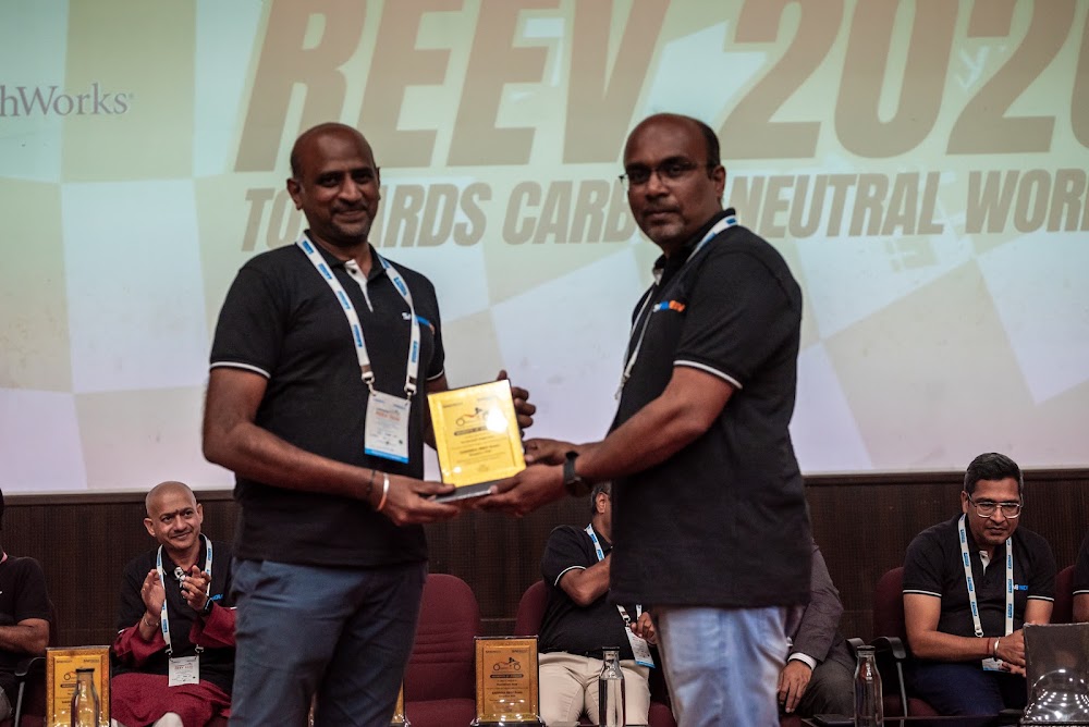 A REEV alumnus presenting an award plaque to a participant on stage at REEV 2026