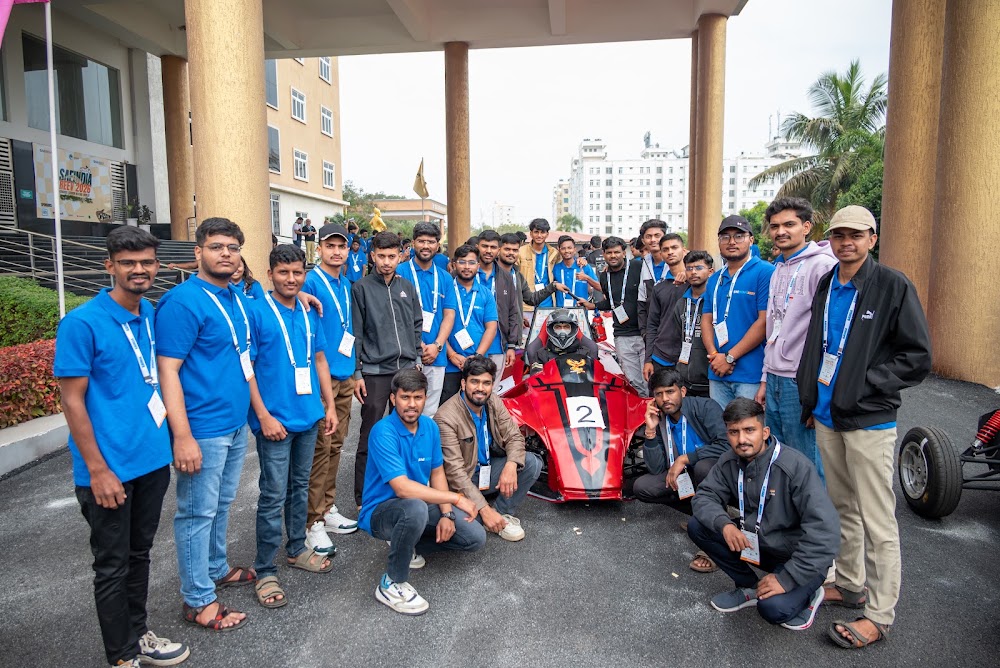 The REEV organizing team posing together with a competition vehicle under the GITAM University colonnade